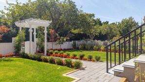 A garden with a white pergola, a paved walkway, and a black railing. - Vancouver Cozy Cove (Vancouver)