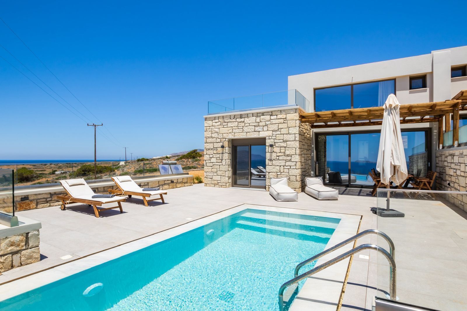 Un área de piscina moderna con sillones de descanso y un muro de piedra, con vistas a un paisaje pintoresco.