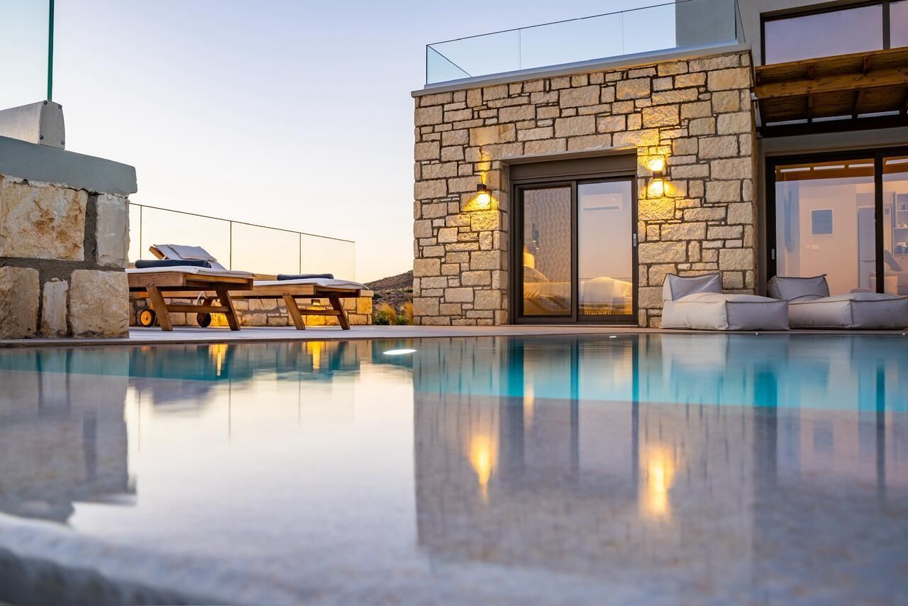 Un espace piscine moderne avec des murs en pierre, des chaises longues et une pièce fermée par des parois de verre.