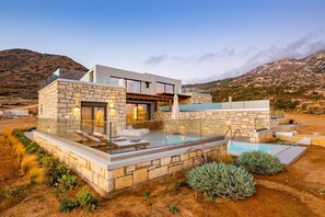 Une maison moderne dotée d’une piscine, de murs en pierre et offrant une vue sur les montagnes.