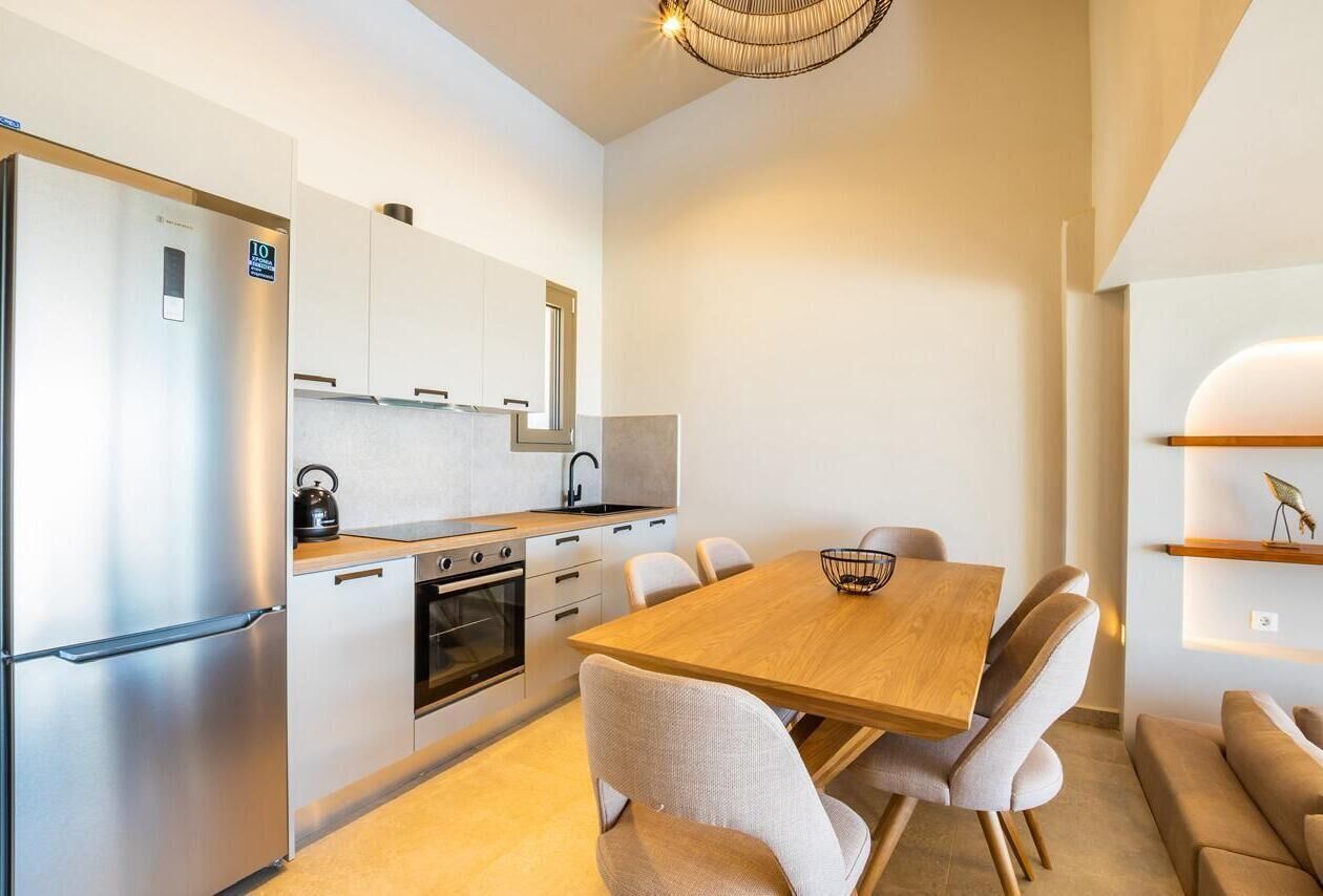 A modern kitchen with a stainless steel refrigerator, a built-in oven, and a wooden dining table with chairs.