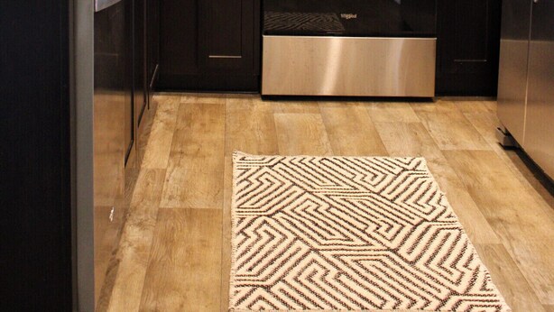Eine moderne Küche mit dunklen Holzschränken, Edelstahlgeräten, darunter Mikrowelle, Backofen und Kühlschrank, einer Granit-Arbeitsplatte und einem dekorativen Teppich.