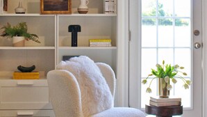 Ein gemütliches Zimmer mit einem weißen Sessel, einem Bücherregal und einer Tür, die nach draußen führt.