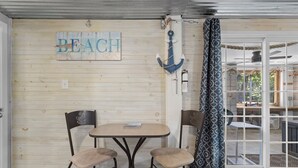 A room with a wooden wall, a table with two chairs, a sign reading "BEACH", and a view through a glass door. - Walk to the Waves: Play & Unwind on the Coast! (Waveland)