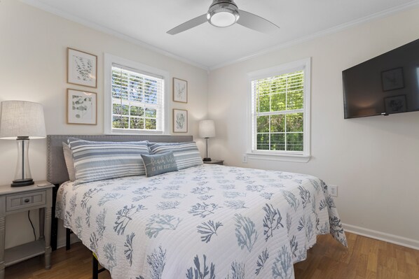 A bedroom with a bed, two bedside tables, a ceiling fan, and two windows with blinds.