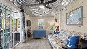 A cozy room with a bed, a sofa, a ceiling fan, and a large window. - Walk to the Waves: Play & Unwind on the Coast! (Waveland)