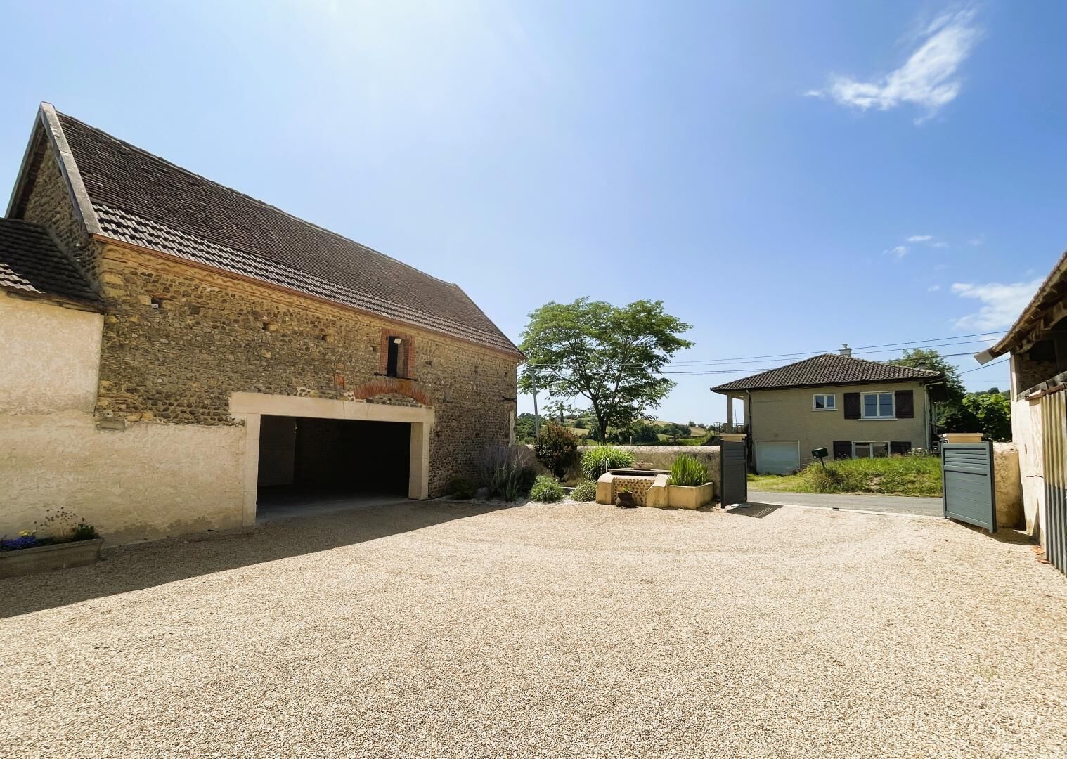 A rural property with a stone barn, a gravel driveway, and a residential house.
