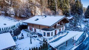 Een met sneeuw bedekte lodge met een balkon, een overdekte patio en uitzicht op het omliggende bos.