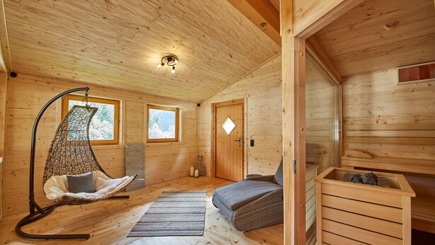 Een gezellig houten kamer met een hangstoel, een bed, een klein tafeltje en een sauna.