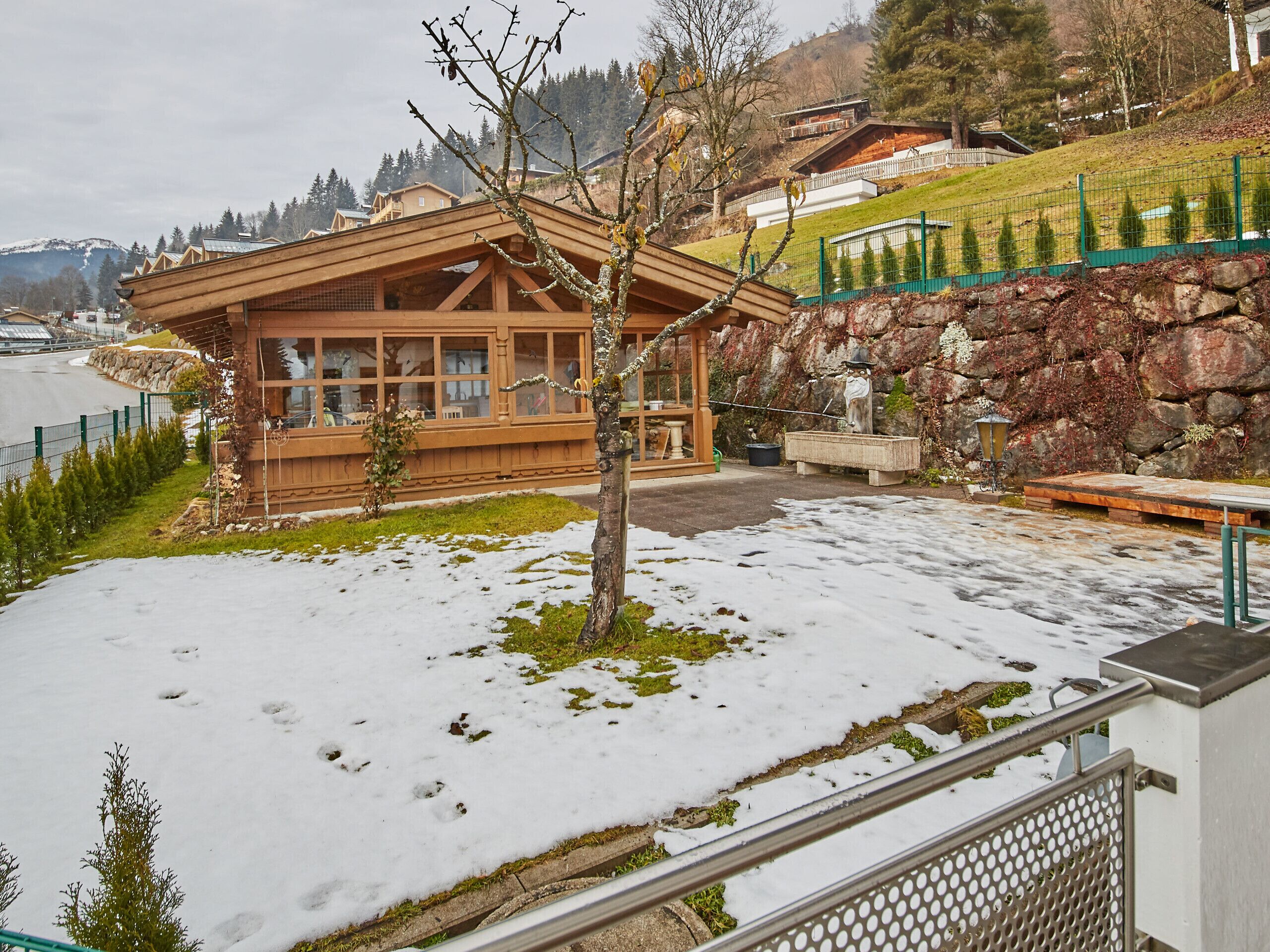 A wooden cabin with large windows, a stone wall, and a snow-covered ground.