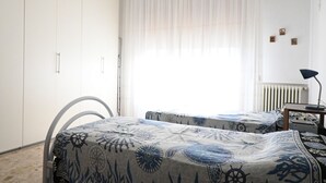 Un dormitorio con dos camas, un armario blanco, una silla y un escritorio con una lámpara.