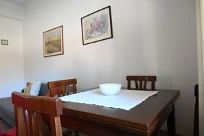 Ein Esstisch mit weißer Platzmatte und einer Schüssel, umgeben von Holzstühlen, in einem Raum mit zwei gerahmten Bildern an der Wand.