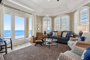 A spacious living room with a large window overlooking the ocean, a comfortable seating area with a sofa and chairs, and a coffee table. - Sandy Shoreline~Ocean Place Resort, Penthouse with insane views (Fernandina Beach)