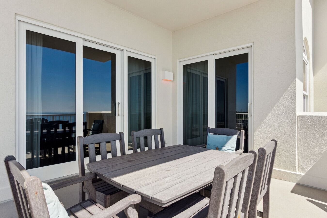 A balcony with a wooden table and chairs, large sliding glass doors, and a view of the sea.