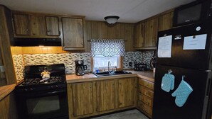 Una cocina con armarios de madera, una estufa negra, un refrigerador y una ventana con cortinas estampadas.