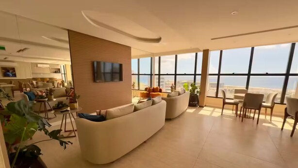 Una sala de estar moderna con un sofá grande, una zona de comedor con sillas y vistas a la ciudad a través de amplios ventanales.