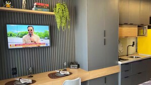 Cocina moderna con armarios grises, encimera de madera y un televisor en la pared mostrando un noticiero.