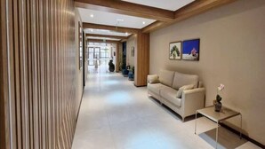 Un moderno vestíbulo de hotel con un largo pasillo, un sofá, una mesa de centro y obras de arte enmarcadas en la pared.