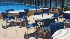Zona de piscina en la azotea con sillas y mesas azules, rodeada de barandillas de vidrio.