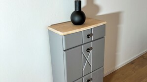 Un meuble gris avec un plateau en bois et un vase noir orné de plumes.