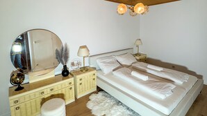 Une chambre avec un plafond en bois, un grand miroir, un lit avec une literie blanche, une table de chevet, une lampe et un tapis moelleux.