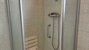 Une cabine de douche fermée par des parois en verre, dotée d’un pommeau de douche à main et d’un robinet fixé au mur.