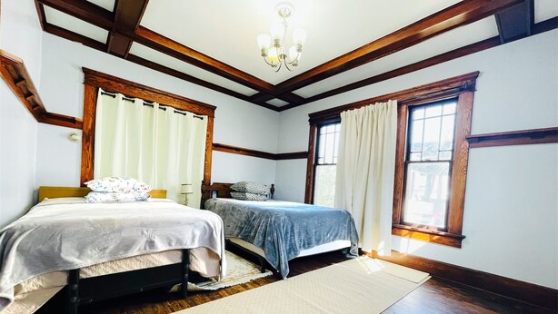 A bedroom with two beds, wooden beams, a chandelier, and large windows with curtains. - Spacious 4-bedroom house with AC, WiFi in  Mansfield (Mansfield)