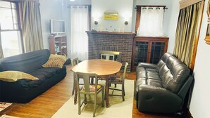 A living room with a black leather sofa, a wooden dining table with chairs, a fireplace, and a television on a stand. - Spacious 4-bedroom house with AC, WiFi in  Mansfield (Mansfield)
