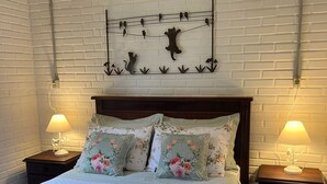 A bedroom with a brick-patterned wall, a wooden headboard, floral pillows, and bedside lamps. - St. Andrew House 3 (Centro Gramado)