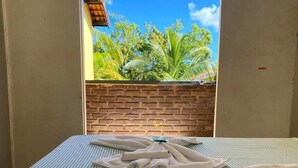 Una habitación con una cama, vistas a la vegetación a través de una ventana y una pared de ladrillo.