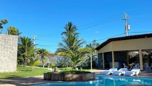 Una piscina con sillones de descanso, rodeada de palmeras y un muro de piedra.