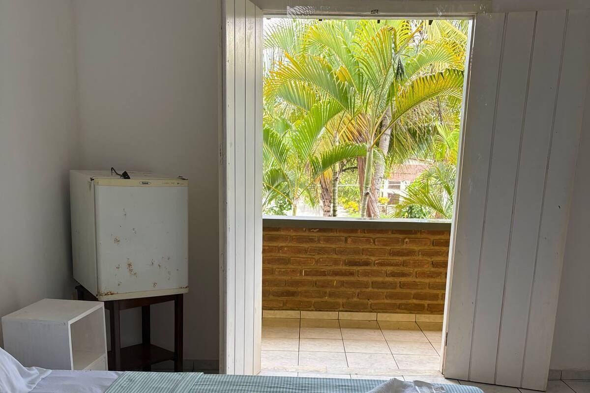 A hotel room with a bed, a television, and a view of palm trees through an open door.