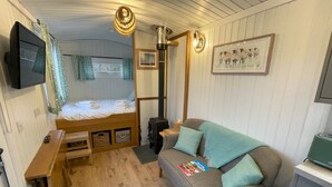 A cozy room with a bed, a sofa, a TV, and a fireplace. - Shepherds  View -  a tiny home that sleeps 2 guests  in 1 bedroom (Glenshee)