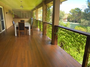 Une terrasse en bois avec une table et des chaises, entourée d’une rambarde et de verdure.