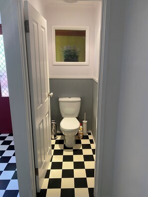 Bathroom with a standard toilet, trash bin, and window.