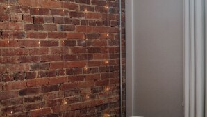 A room with a brick wall, a bed with a patterned blanket, and a white door. - Charming 2-bedroom apartment with AC, WiFi in lovely Mifflinburg (Mifflinburg)