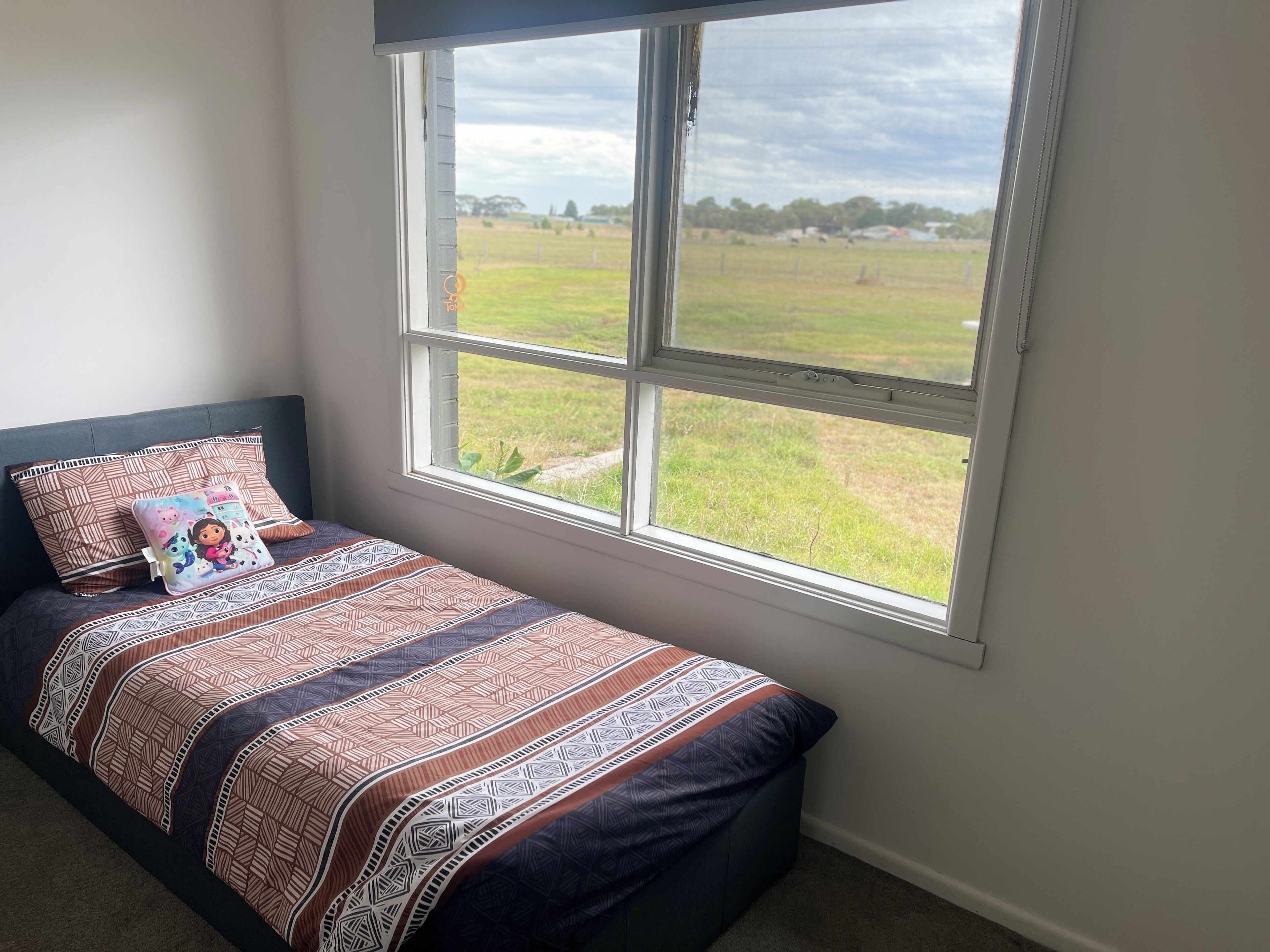 A bedroom with a bed, pillows, and a window with a view of a field.