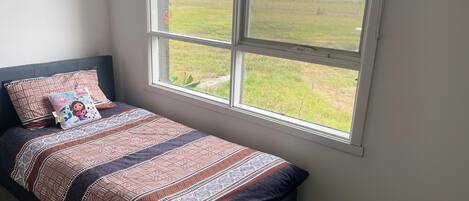 A bedroom with a bed, pillows, and a window with a view of a field.