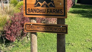Une enseigne en bois pour Sandhu Farms, avec un logo représentant une montagne et une maison, et une plus petite enseigne en dessous indiquant « 122, chemin Wellington, Moolap ».