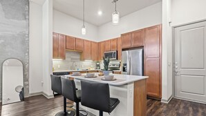 A modern kitchen with wooden cabinets, a central island with bar stools, stainless steel appliances, and pendant lighting.