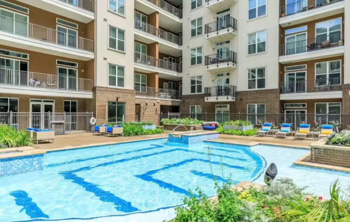 A multi-story residential building with a central swimming pool, balconies, and outdoor seating areas.