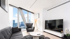 Ett modernt vardagsrum med en soffa, fåtölj, TV och utsikt över staden.