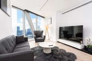 Ein modernes Wohnzimmer mit Sofa, Sessel, Fernseher und Blick auf die Stadt.