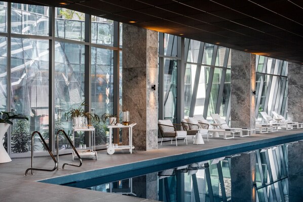 Relax in a sleek, contemporary pool area with lounge chairs and tables, surrounded by large windows offering views of the surrounding area.