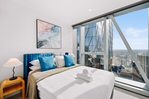 Relax in a spacious room with a large bed, a wooden nightstand, and a panoramic city view.