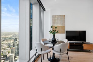 Enjoy a panoramic city view from the comfort of this stylish living room, featuring a round dining table, flat-screen TV, and a large abstract painting.