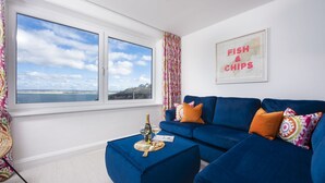 A room with a blue sofa, a small table with a bottle and glasses, a colorful curtain, and a wall with a 'FISH & CHIPS' sign.