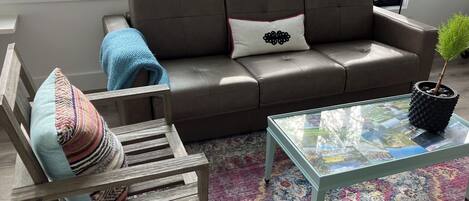 Un salon moderne avec un canapé en cuir marron, une table basse en verre et un tapis à motifs.