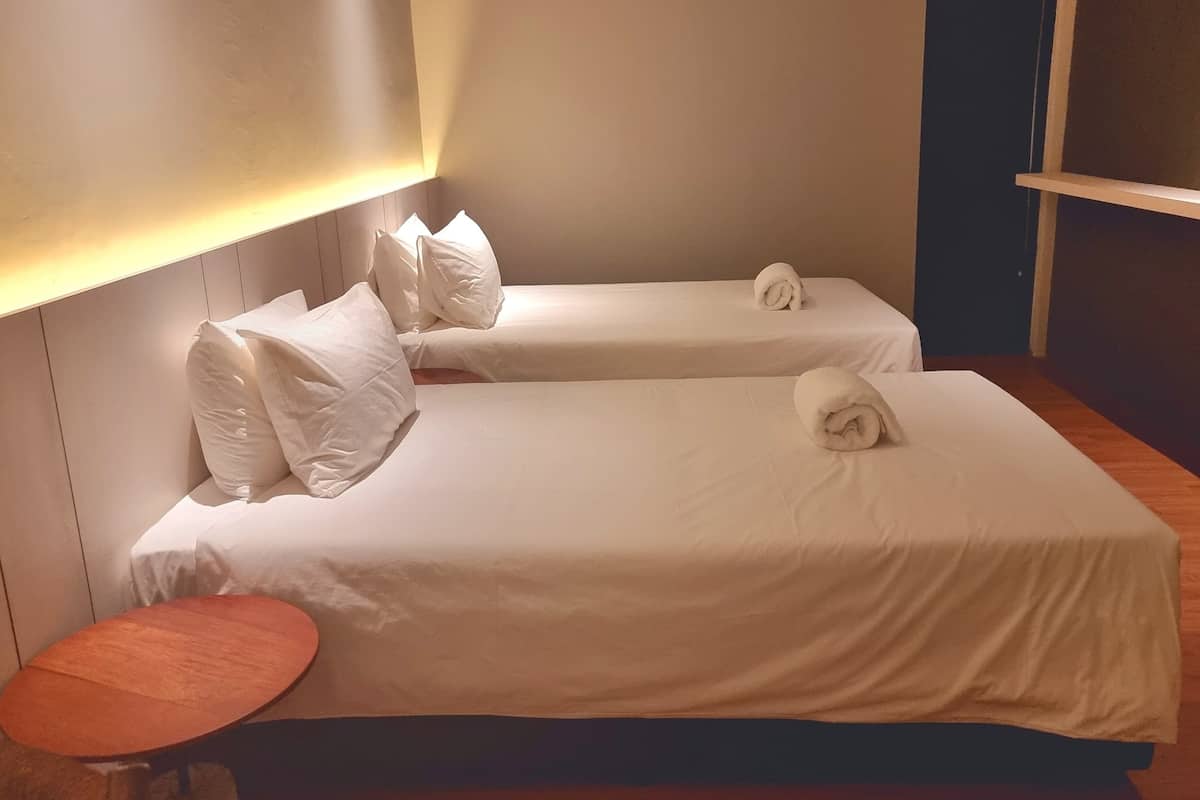 Hotellihuone, jossa on kaksi erillistä sänkyä. Jokaisessa sängyssä on valkoiset lakanat ja tyynyt, huoneessa on myös puinen yöpöytä ja pieni pyöreä pöytä.