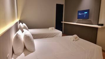 Une chambre d’hôtel avec deux lits simples, chacun équipé d’un oreiller et d’une serviette portant le nom « ROXY ». Un téléviseur à écran plat est fixé au mur, au-dessus d’une étagère.